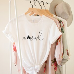 May include: White t-shirt with a black graphic of a castle and the word "magical" in cursive.