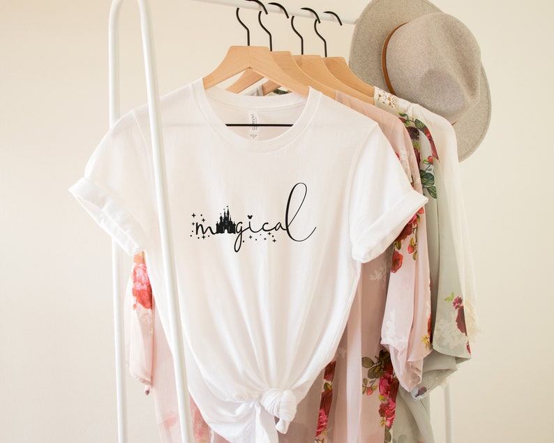 May include: White t-shirt with a black graphic of a castle and the word "magical" in cursive.