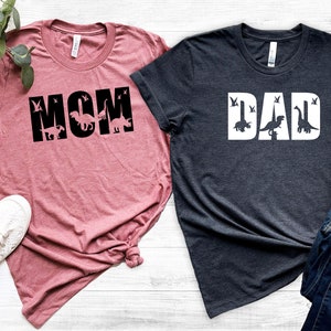 May include: Two t-shirts, one pink and one dark gray, with the words "MOM" and "DAD" in large white letters.  Dinosaurs are incorporated into the letters.