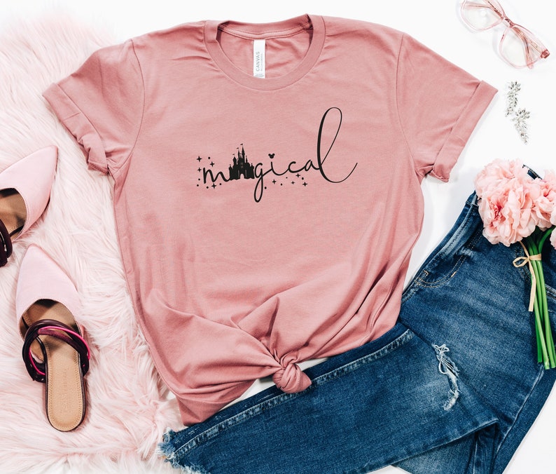 May include: A pink t-shirt with a black silhouette of Cinderella's castle and the word "magical" written in cursive.