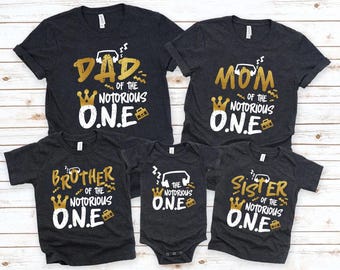 May include: A set of four black t-shirts with gold text and graphics. The shirts say "Dad of the Notorious O.N.E." "Mom of the Notorious O.N.E." "Brother of the Notorious O.N.E." and "Sister of the Notorious O.N.E."