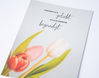 May include: A card with a light gray background and the text "UNENDLICH geliebt. VOLLKOMMEN begnadigt." in black. Three tulips are shown in the bottom right corner of the card. The tulips are pink, white, and orange.