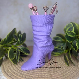 May include: A lavender boot-shaped pen holder with a high heel and textured design. The pen holder contains several decorative pens with pink and silver accents. The text "Exotic Hands" and "Sublimation, Laser, Blanks & More" are visible on the boot.