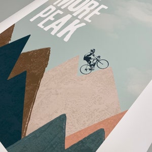 May include: A motivational poster with a cyclist riding up a mountain with the text "ONE MORE PEAK" in white letters on a light blue background.