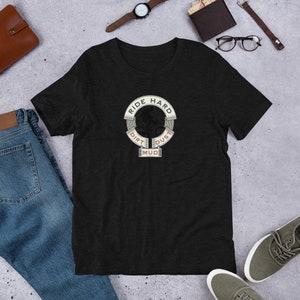 Peut inclure: T-shirt noir avec un graphique d'un cycliste de montagne traversant la terre, la boue et la poussière. Le graphique est entouré d'un cercle avec le texte "Ride Hard" en haut et "Dirt, Dust, Mud" en bas.