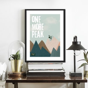May include: A framed print with a mountain landscape and a cyclist jumping over a peak. The text "ONE MORE PEAK" is printed in white on a light blue background.