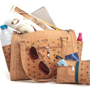 May include: A cork handbag with a blue and white patterned design. The bag is open and filled with items, including a water bottle, sunglasses, and a passport. The bag has a zipper closure and two handles. There is also a smaller cork pouch with a green zipper.