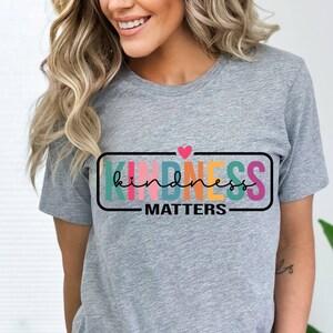 May include: A gray t-shirt with a rainbow colored graphic that says "kindness matters" with a small pink heart above the word "kindness".
