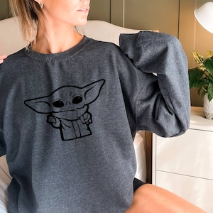 May include: A gray sweatshirt with a black graphic of a character from the Star Wars franchise, known as "The Child" or "Baby Yoda".