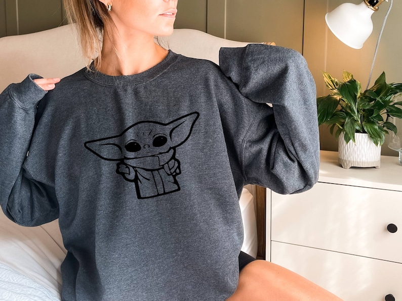 May include: A gray sweatshirt with a black graphic of a character from the Star Wars franchise, known as "The Child" or "Baby Yoda".
