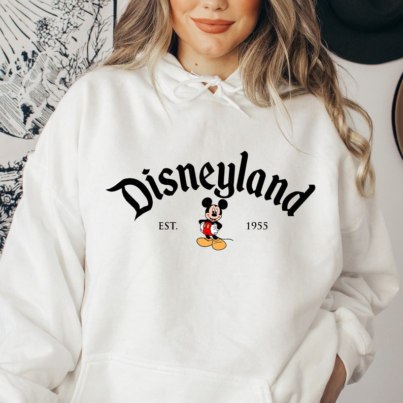 May include: White hooded sweatshirt with a black Disneyland logo and Mickey Mouse graphic. The logo reads "Disneyland" with "EST. 1955" underneath.