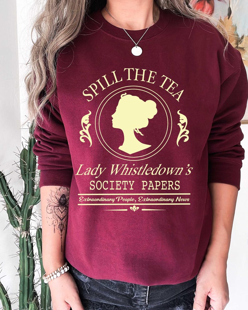 May include: Burgundy sweatshirt with the text "Spill the Tea" in gold lettering, featuring a silhouette of a woman's profile. Below the text is "Lady Whistledown's Society Papers" and "Extraordinary People, Extraordinary News".