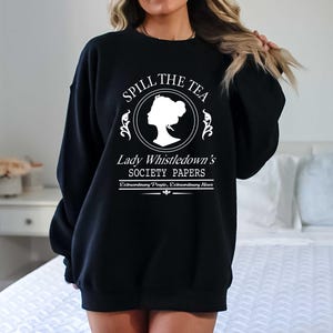 May include: Black sweatshirt with white text that reads "Spill the Tea" above a silhouette and "Lady Whistledown's Society Papers". The sweatshirt is a crew neck style.