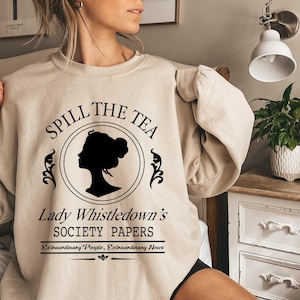 May include: Beige sweatshirt with the text "Spill the Tea" above a black silhouette of a woman's profile within a circle. Below, it reads "Lady Whistledown's Society Papers" and "Extraordinary People, Extraordinary News".