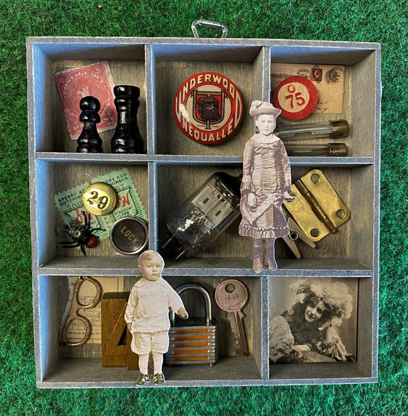 May include: A vintage-style wooden box with nine compartments, each filled with various objects, including a miniature doll, a vintage toy, a lock, a vintage stamp, a vintage game piece, a vintage bottle, a vintage key, a vintage button, and a vintage pin. The box is decorated with a vintage label that reads "Underwood".