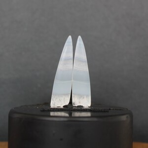 Puede incluir: Un par de pendientes de ágata blanca con forma de lágrima puntiaguda. Los pendientes tienen un patrón de bandas superpuestas con un color blanco lechoso translúcido.