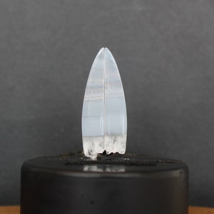 Puede incluir: Un par de cabujones de ágata blanca con un patrón de bandas. Los cabujones son puntiagudos en la parte superior y tienen una parte inferior rugosa y texturizada.