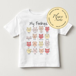 May include: White t-shirt with a graphic of cats expressing different emotions. The text "My Feelings" is printed above the graphic. Each cat has a different facial expression and a word describing the emotion below it.