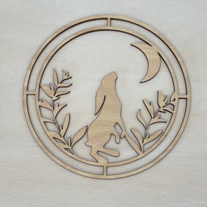 May include: A wooden circle with a cutout design of a rabbit, crescent moon, and foliage. The design is in a natural wood colour.
