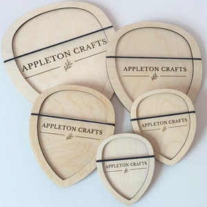 Può includere: Quattro targhe in legno con il testo "APPLETON CRAFTS" e un piccolo disegno a foglia. Le targhe sono di diverse dimensioni e forme, alcune sono rotonde e altre a forma di cuore. Ogni targa è circondata da un elastico nero.