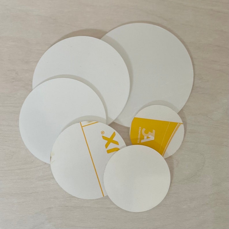 May include: A set of six white round filter papers of varying sizes. The largest filter paper is 12 inches in diameter. The smallest filter paper is 3 inches in diameter. The filter papers are arranged in a circle on a light brown wooden surface.