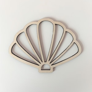May include: A wooden seashell cutout in a light brown colour. The seashell has a detailed design with multiple curves and lines.