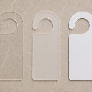 May include: Three rectangular door hangers with a circular hook at the top. The first hanger is made of clear transparent material, the second is made of a semi-transparent frosted material, and the third is made of a solid opaque white material.