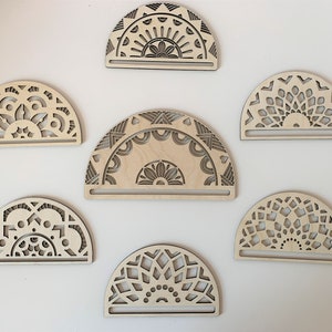 May include: Six wooden half-circle ornaments with intricate laser-cut mandala designs. The ornaments are made of light brown wood and have a natural finish.