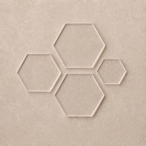 May include: A set of four clear acrylic hexagon shapes arranged in a cluster. The collection includes two larger hexagons of equal size, one medium hexagon, and one smaller hexagon, all featuring smooth, transparent surfaces and defined edges.