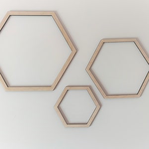 Peut inclure: Trois cadres hexagonaux en bois de différentes tailles, disposés en ordre décroissant de gauche à droite, sur un fond blanc.