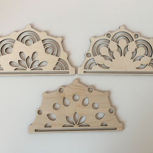 May include: Three unfinished wooden cutouts in the shape of a half-circle with intricate designs. The designs feature a central leaf motif surrounded by circles and other geometric shapes.