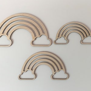 Pode incluir: Três peças de decoração de parede de arco-íris de madeira com nuvens. O arco-íris maior tem três camadas, o arco-íris do meio tem duas camadas e o arco-íris menor tem duas camadas.