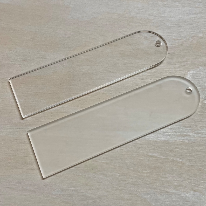 May include: Two clear acrylic bookmarks, one with a rounded top and one with a straight top. Both bookmarks are blank and ready for personalization.