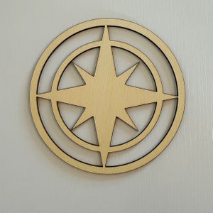May include: A wooden cutout of a compass rose with a star in the centre. The compass rose has two concentric circles around the star.