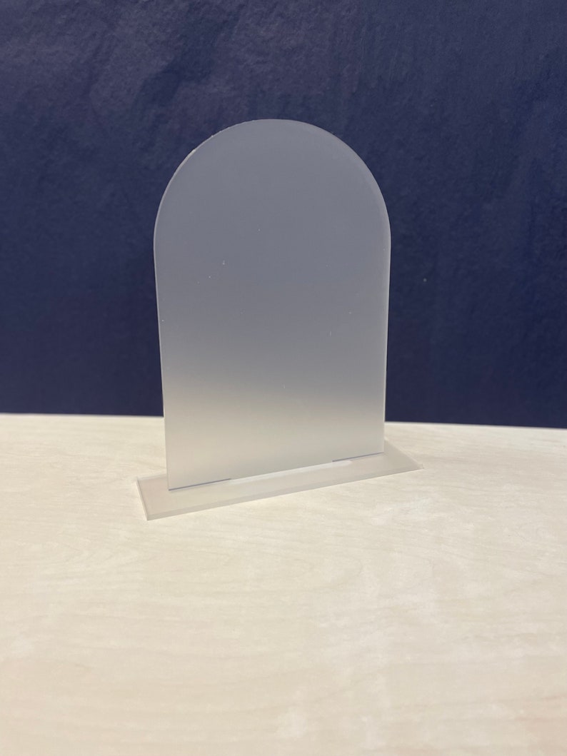 K&ouml;nnte beinhalten: Ein mattierter Acryl-Bogenst&auml;nder mit abgerundeter Oberseite und flachem Sockel. Der St&auml;nder ist aus klarem Acryl gefertigt und hat eine matte Oberfl&auml;che.