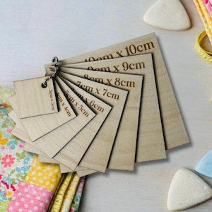 May include: A collection of wooden squares, each labelled with its dimensions in centimetres, linked by a metal ring. Sizes vary from 3cm x 5cm to 10cm x 10cm. The natural wood grain is visible on each square.