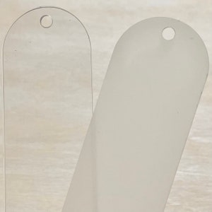 May include: Two blank, oval-shaped, plastic tags with a hole at the top. The tag on the left is clear, while the tag on the right is frosted.