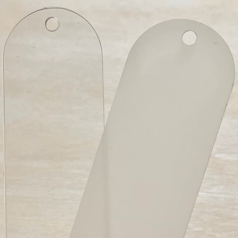 May include: Two blank, oval-shaped, plastic tags with a hole at the top. The tag on the left is clear, while the tag on the right is frosted.