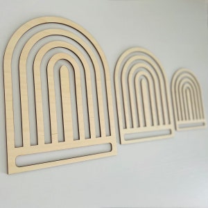 Op de afbeelding: Drie houten regenboogbogen van verschillende grootte, gerangschikt in aflopende volgorde van links naar rechts. De bogen zijn gemaakt van dun, gelaagd hout en hebben een natuurlijke, lichtbruine kleur.