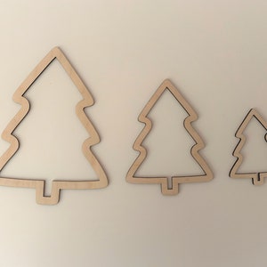 Könnte beinhalten: Drei hölzerne Weihnachtsbaum-Ausschnitte in verschiedenen Größen. Die Bäume haben alle die gleiche Form mit einer einfachen, abgerundeten Umrandung. Sie sind aus Naturholz gefertigt und haben eine hellbraune Farbe.