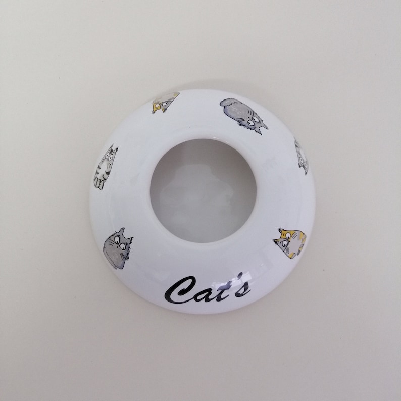 May include: White ceramic ring holder with a cat design and the word "Cat's" printed on the bottom.
