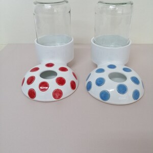 May include: Two white ceramic pet food and water bowls with red and blue polka dots. Each bowl has a clear glass jar on top.