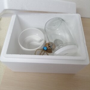 May include: A white polystyrene box containing a white ceramic mug, a clear glass jar, and a small wooden tag with the text "DAISY CERAMIC" on it.