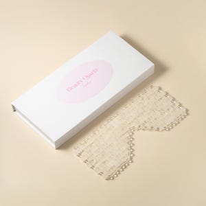 May include: A white quartz eye mask with a textured surface. The mask is packaged in a white box with the text "Beauty Quartz London" printed on it.