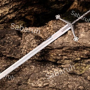May include: A long, silver sword with an ornate handle and crossguard, set against a textured, brown background. The crossguard has decorative details, and the blade is sharp and reflective. The text "Sabaruh" is visible on the image.