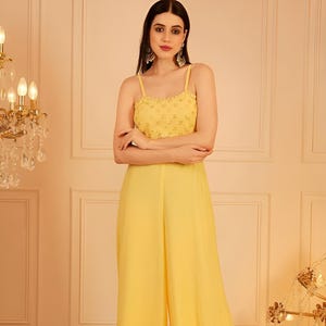 Pode incluir: Macac&atilde;o amarelo com corpete com contas e cal&ccedil;as de perna larga. A parte superior apresenta al&ccedil;as finas e um design detalhado. As cal&ccedil;as s&atilde;o de tecido liso e fluido. O traje &eacute; de cor brilhante e lisa.