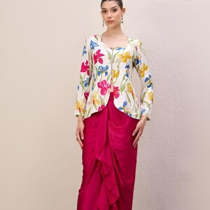 May include: A two-piece outfit comprising a floral print jacket and a fuchsia skirt. The jacket has a square neckline and a zip closure. The skirt features a draped design. The floral print includes pink, blue, and yellow flowers on a white background.