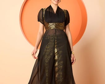 Op de afbeelding: Een zwart en goud formele outfit. De top heeft een doorschijnende overlay met korte mouwen en een goudkleurige band in de taille. De bijpassende broek heeft een goudkleurig patroon. De outfit wordt gedragen met gouden sandalen.