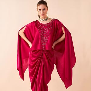 May include: A magenta flowing draped skirt with a matching magenta top featuring a beaded rose design. The top has a cape-like sleeve.