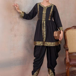 May include: A black tunic and dhoti trouser set featuring gold metallic floral brocade trim along the neckline, centre front, cuffs, and hem. The tunic has long sleeves and a gathered waist, while the dhoti trousers feature a draped silhouette.